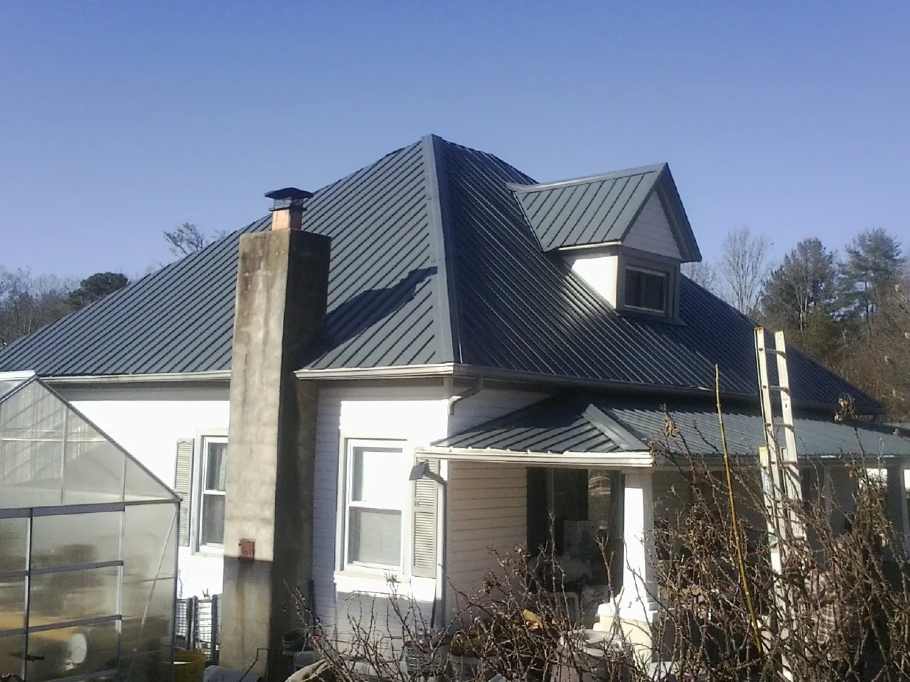 Dark blue standing seam metal roof on a white farmhouse with dormer — Slate & Tile Roof Repair by Roofing Brothers in Athena