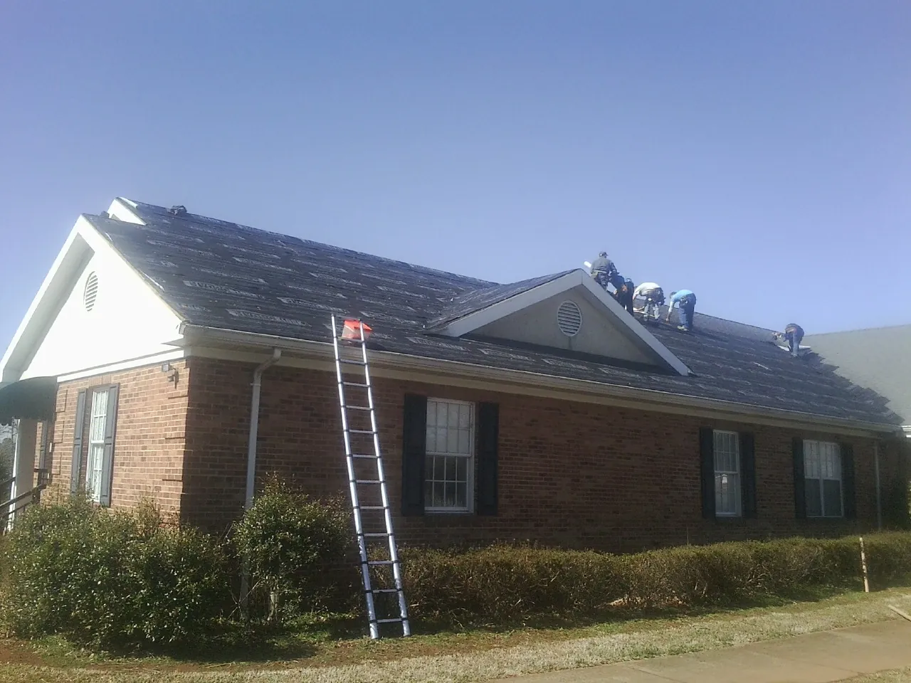 Crew tearing shingles off a brick ranch roof with a ladder set — Emergency Roof Repair work by our crew in Athena