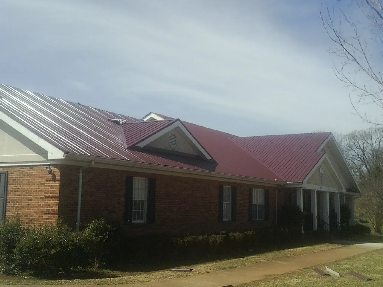 Red metal roof with gabled entries on a long brick building, from a Hail Damage Roof Repair job in Athena