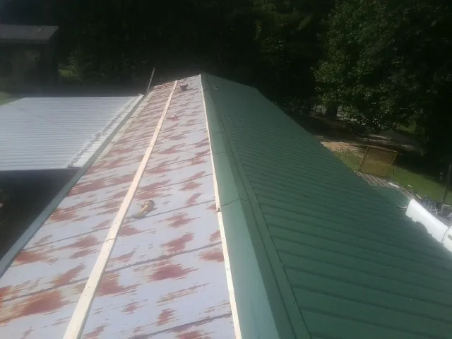 Old rusted panels beside newly installed green metal roofing — Wind Damage Roof Repair by Roofing Brothers in Athena