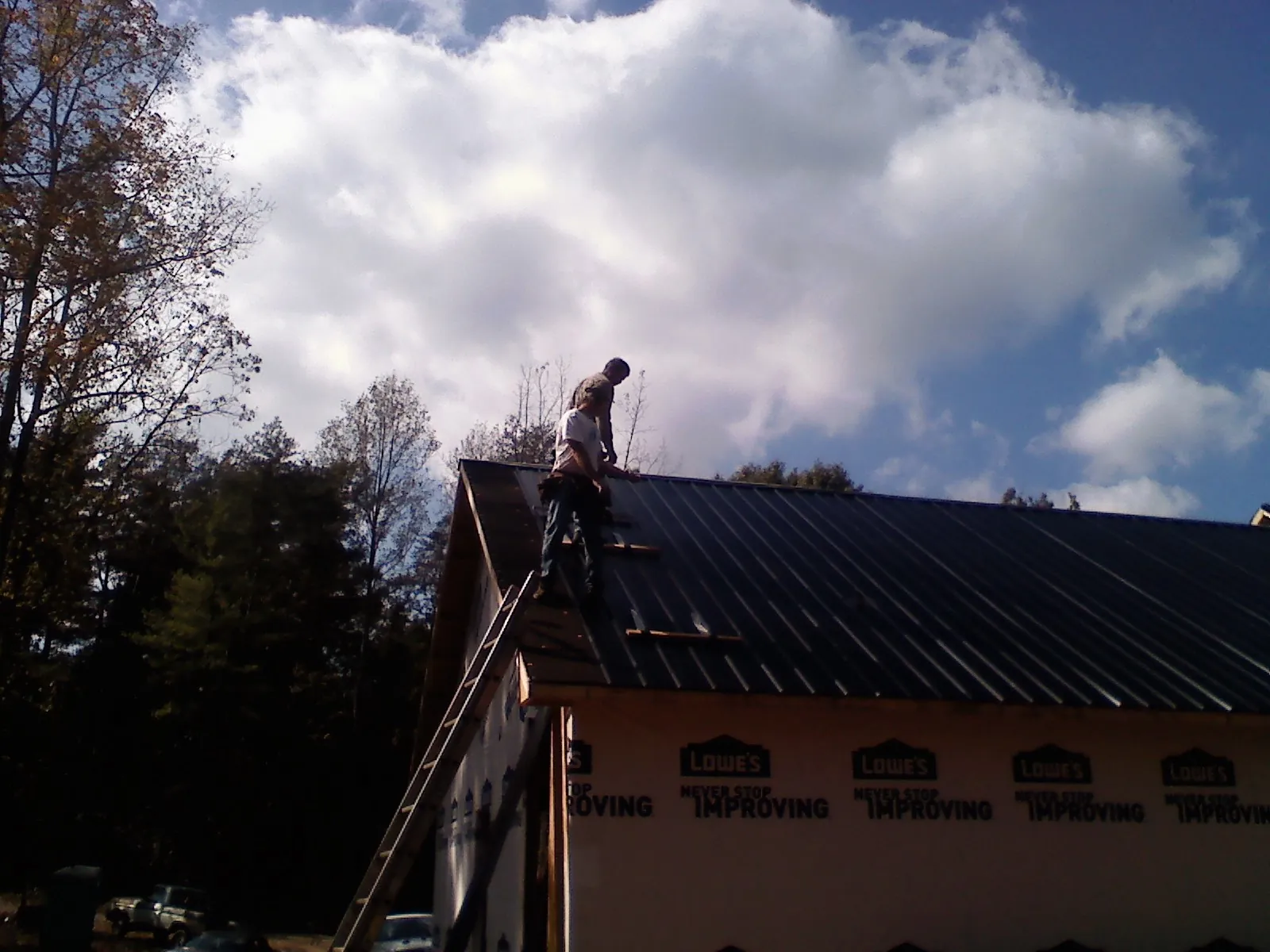 Roofer fastening dark metal panels high against a cloudy sky, from a Roof Inspection job in Athena