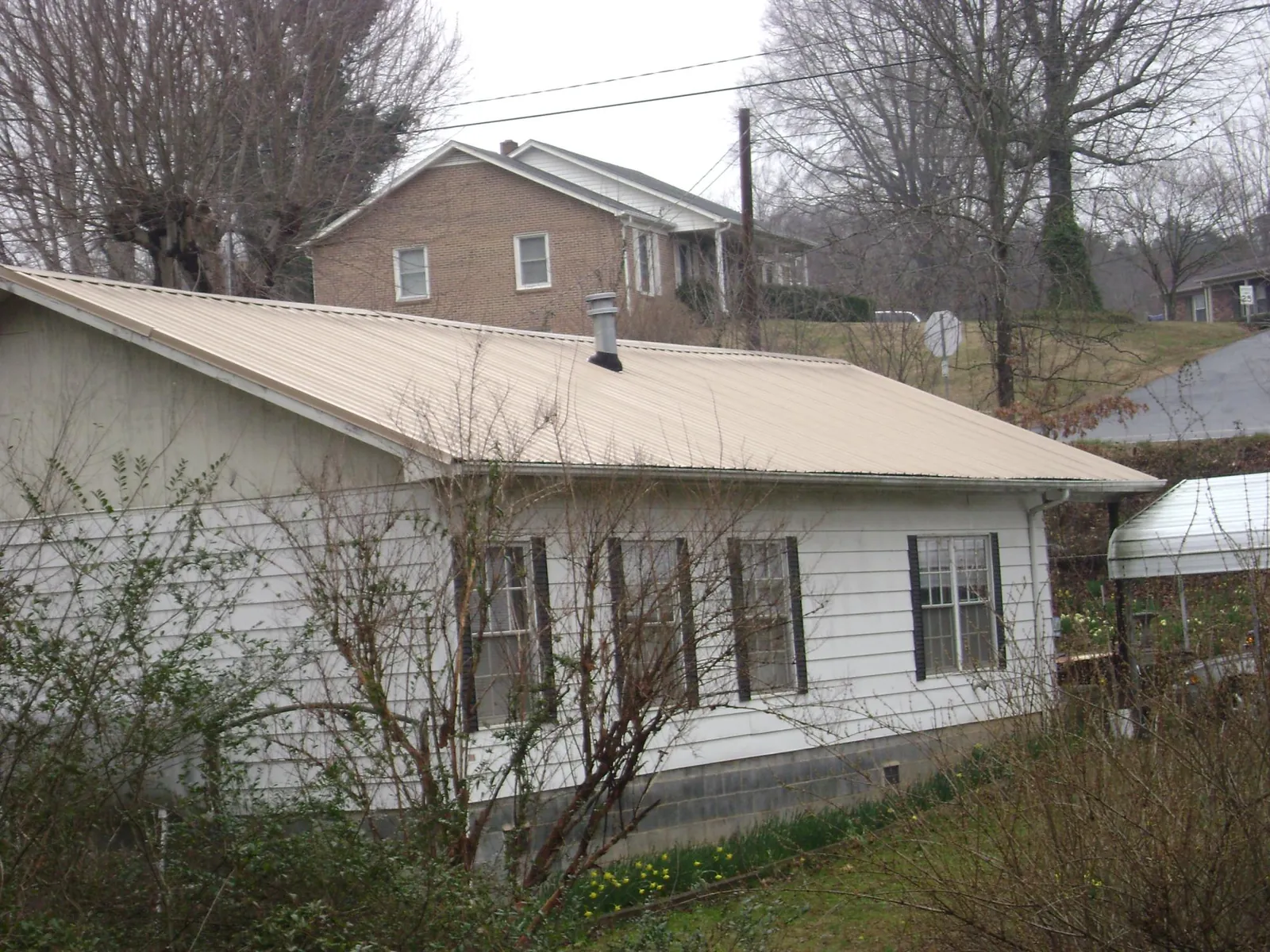 Tan metal roof on a white sided house set into a hillside — Commercial Roofing by Roofing Brothers in Athena
