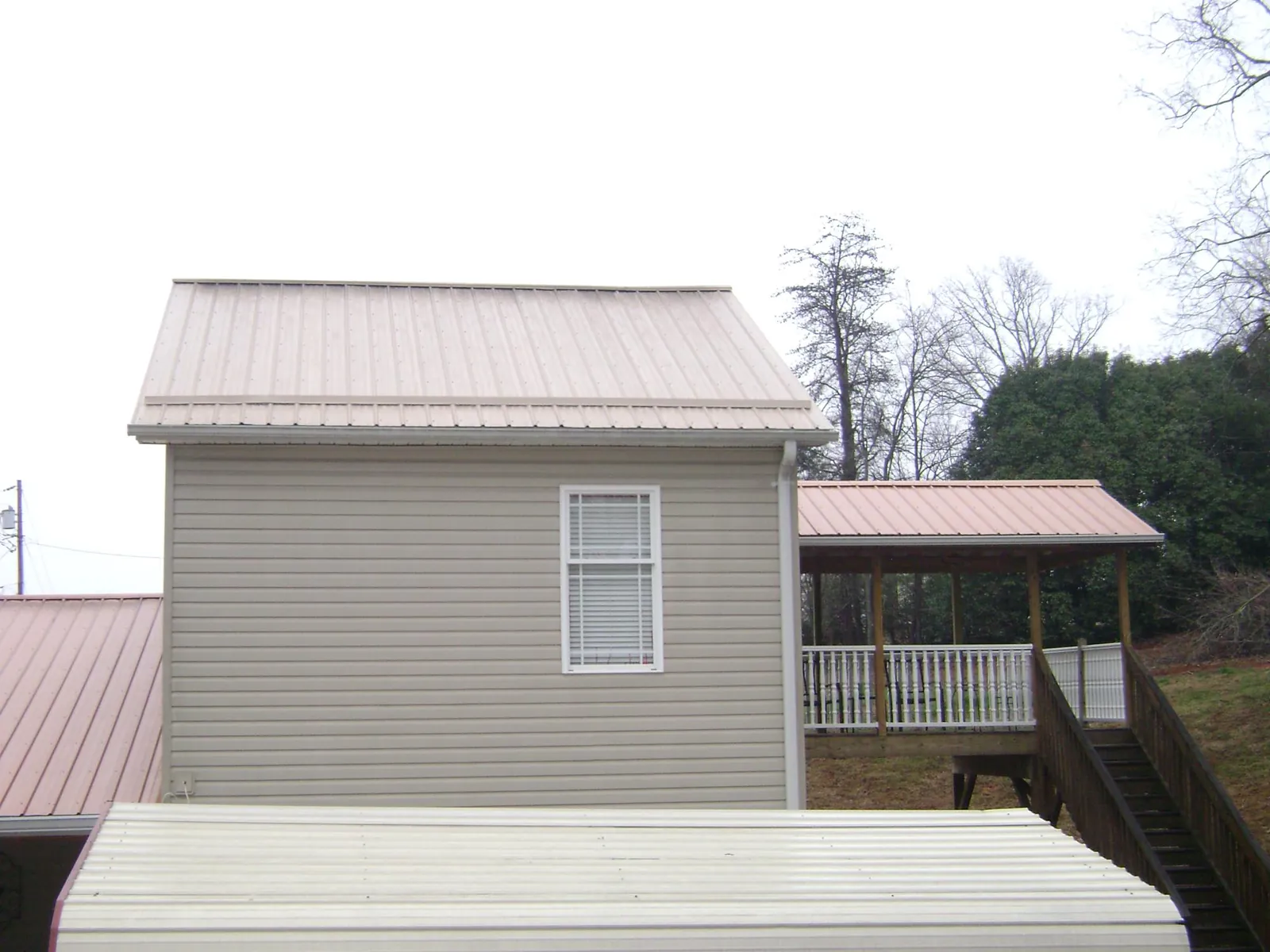 Tan metal roofs on a two story addition and attached porch, from a Roof Replacement job in Athena